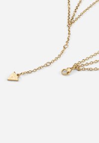 Gouden metalen ketting met een driehoekige hanger met gegraveerd logo, delicate kettingontwerp en een karabijnsluiting.