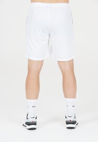 Bakifrån av en person som bär vita sportshorts, vita strumpor med svarta texter och vita och svarta idrottsskor på en vit bakgrund.