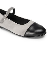 Bailarina de ante gris con puntera de cuero negro, que presenta una correa con hebilla plateada. Textura suave, diseño de perfil bajo.