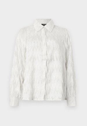 Camisa blanca de botones con un patrón texturizado de zigzag y acentos deshilachados, con un cuello clásico y mangas largas.