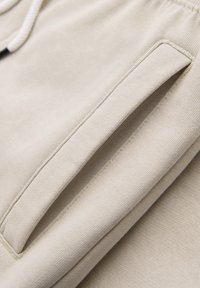 Tela beige con un primer plano de un bolsillo rectangular cosido en ropa casual, mostrando tejido texturizado y costuras limpias.