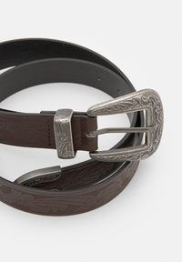 Brun læderbælte med præget blomsterdesign og en udsmykket sølvmetalspænde og løkke, snoet på en hvid baggrund.