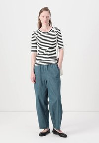 Schwarz-weiß gestreifte Bluse mit Dreiviertelärmeln, kombiniert mit locker sitzenden blauen Jeans und schwarzen Ballerinas. Einfaches Design, lässiger Stil.