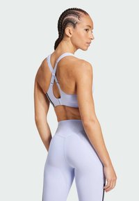 Lilafarget sports BH med kryssryggdesign, justerbare stropper og et utskjæringsdetalj på baksiden, parret med matchende høyt liv leggings.