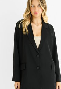Black blazer made from smooth fabric, featuring a single-breasted design with two buttons, notched lapels, and side pockets.