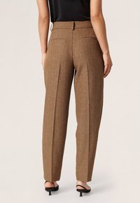 Brunatne, strukturalne spodnie o dopasowanym kroju z wysokim stanem, z dwiema tylnymi kieszeniami i prostymi nogawkami, w połączeniu z czarnymi sandałami na obcasie.