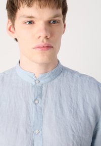 Himmelblaues Hemd mit Button-Down-Kragen aus strukturiertem Stoff, mit einer Knopfleiste vorne und minimalistischem Design.
