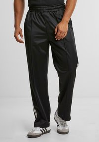 Black, lightweight athletic pants with an elastic waistband and side stripes. Smooth texture and straight fit provide comfort and ease of movement.
