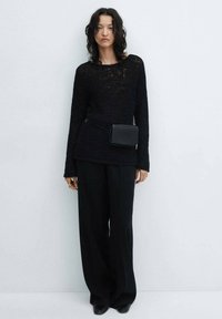 Černý pletený svetr s dlouhými rukávy, doplněný volnými černými kalhotami. Malá černá kabelka na kříž se nosí kolem pasu. Minimalistický design.