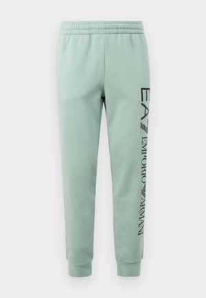 Mint green joggers made from soft fabric, featuring an elastic waistband and a printed logo in black along the left leg.