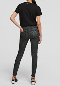 Camiseta negra de manga corta, combinada con jeans ajustados de color gris oscuro que presentan bolsillos traseros texturizados y un ligero brillo.