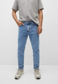 Jeans in denim azzurro chiaro con vestibilità dritta, caratterizzati da una vita a mezza altezza e un design a cinque tasche, abbinati a una t-shirt grigia e sneakers beige.