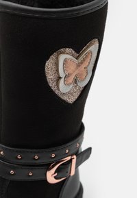Svart mockastövlar med en silver- och rosé-guld fjärilsdetalj på ett hjärtapplikation, med en nubbad svart rem och spännardetalj.