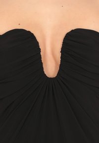 Abito nero senza spalline con profondo scollo a V, caratterizzato da tessuto arricciato per aggiungere texture e una silhouette fluida. Materiale liscio.