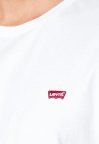 White cotton t-shirt featuring a small red embroidered Levi's logo on the left side of the chest. Crew neck design with a smooth texture.
