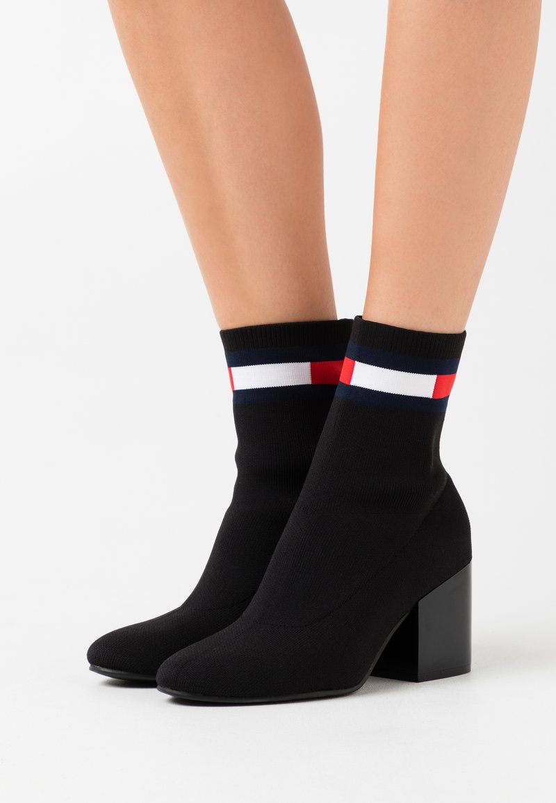 Bottine noire en maille avec un bout effilé et un talon bloc, dotée d'un revers rayé multicolore rouge, blanc et marine. Texture en maille lisse.