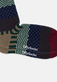 Calcetas coloridas que presentan una mezcla de patrones, incluyendo diseños a cuadros y rayas, en tonos de azul marino, verde, burdeos y beige. Logo de "DillySocks" visible.