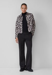 Veste imprimée léopard avec un design structuré, associée à un col roulé noir à côtes et un pantalon noir ajusté. Des chaussures noires complètent le look.