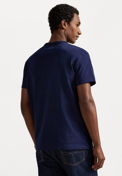 Tengerészkék pamut póló rövid ujjakkal, kerek nyakkal és sima textúrával. Egyszerű, díszítések nélküli hátoldali dizájnnal rendelkezik.