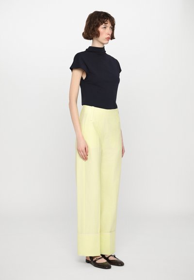 Haut col roulé bleu marine à manches courtes, associé à un pantalon large taille haute jaune clair et des chaussures Mary Jane noires.