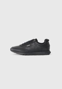Black low-top sneaker with lace-up front, textured details, and "HUGO" logo on side, shown in profile on white background.
