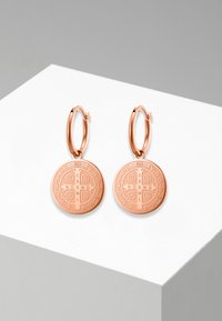 Roze gouden oorringen met ronde bedels voorzien van gegraveerde symbolen en tekst. Gladde oppervlakte met een gepolijst afwerking.