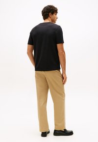 Svart bomulls-t-shirt med korta ärmar och rund halsringning, kombinerad med beige byxor med raka ben och svarta blankpolerade loafers.