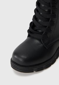 Μαύρη δερμάτινη μπότα στοκ με στρογγυλή μύτη, υφασμένη ένδυση με κορδόνια και χνουδωτή καουτσούκ σόλα με μοτίβο για καλύτερη πρόσφυση.