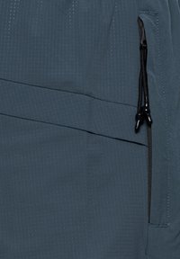 Mørkeblåt stof med subtilt gittermønster, der viser en lynlåslomme med sorte lynlåstrække på højre side.