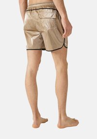 Pantaloncini da bagno marrone chiaro con finitura lucida, cintura elastica, piping nero e tasca sul retro. La vista frontale mostra un taglio laterale per il movimento.
