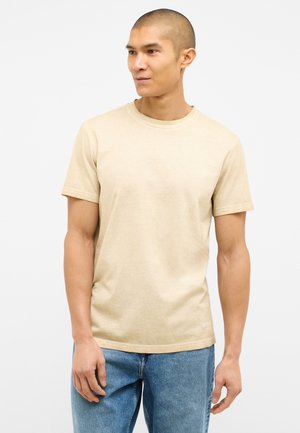 T-shirt beige à manches courtes en coton doux, avec un col rond et une coupe décontractée. Porté avec un jean en denim bleu clair.