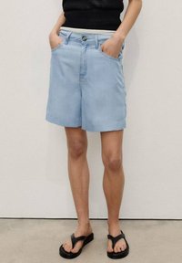 Vaaleansiniset rentomalliset farkkushortsit, joissa on vyölenkit, etutaskut ja napillinen suljenta, yhdistettynä mustiin tasapohjaisiin sandaaleihin.