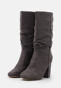 Bottines en suède gris avec un dessus décontracté, bout rond et un large talon block. Texture lisse avec des détails de couture subtils au niveau de la cheville.