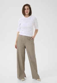 Maglione bianco a maglia con motivo a zig zag testurizzato, abbinato a pantaloni larghi in tono marrone chiaro a vita alta con fessura laterale e dettagli delle tasche.