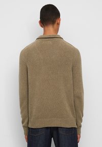 Pull en maille marron avec col haut, poignets et ourlet côtelés. Présente une finition texturée et une coupe décontractée, montré de l'arrière.