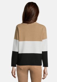 Sweter z prążkowanego dzianiny w paski w kolorach brązowym, białym i czarnym. Posiada długie rękawy i luźny krój. Brak zauważalnych elementów metalowych lub akcentów.