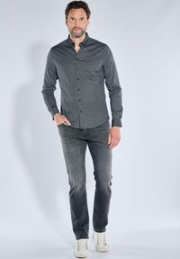 Hemd in Dunkelgrau mit einem subtilen Muster, kombiniert mit verwaschenen grauen Jeans und weißen Sneakers, was einen lässigen, abgestimmten Look kreiert.