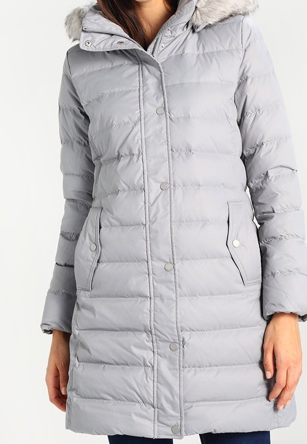 Lyst grå polstret jakke med en hætte foret med faux pels, trykknaplukning, sidelommer og kviltet tekstur. Lange ærmer med elastiske manchetter.