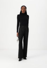 Top noir à manches longues et pantalon large avec une texture légère. Les accessoires incluent un petit sac à main métallique. Modèle portant des chaussures à bout pointu.