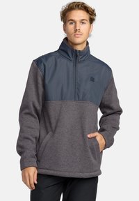 Polarowy sweter w ciemnoszarym i granatowym kolorze z półzamkiem, wysokim kołnierzem, kieszenią typu kangur oraz fakturowanym materiałem powyżej talii.