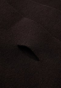 Tissu brun foncé avec une texture douce, présentant un petit détail de découpe arrondie ou de poche. L'accent est mis sur la surface du tissu.