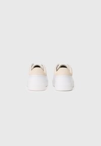 Et par hvite lavt opp sneakers med beige semsket h�ælbelegg, sett fra baksiden på en hvit bakgrunn.