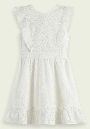 Weißes Lochmusterkleid mit Rüschensäumen, strukturiertem Muster und schwingendem Saum. Kombiniert mit braunen, Riemchensandalen, die Knöchelbindebänder haben.