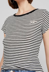 Black and white striped t-shirt featuring a round neckline, short sleeves, and an embroidered logo on the chest. Soft fabric texture.