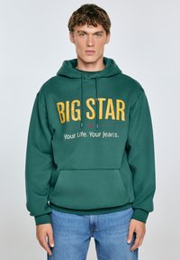 Zelena kapuca s puloverjem z rumenim napisom "BIG STAR" in manjšim napisom spodaj. Fleece material, sprednji žep, rebrasti manšeti.