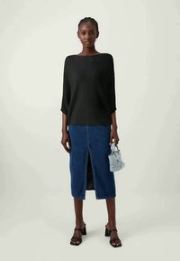 Black ribbed top, knee-length denim skirt with front slit, and a light blue handbag. Model wears black strappy heels, neutral background.