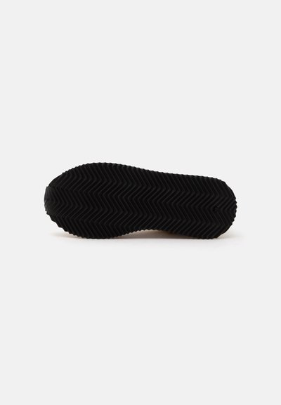 Semelle de chaussure noire avec un motif de bande de roulement en zigzag, présentée à plat sur fond blanc uni.