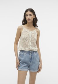 Top beige de punto con un patrón similar al encaje y pequeños botones, combinado con shorts de denim azul claro con cinturilla elástica y puños enrollados.