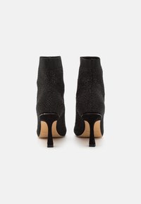 Stivali neri alla caviglia con una tomaia tessuta e strutturata e un colletto in tessuto liscio. Presentano un tacco di 5 cm e un design a punta.