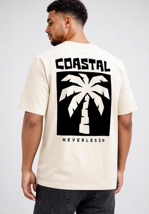 Man wearing off-white T-shirt with black graphic of a palm tree and text "COASTAL" above and "NEVERLESS" below on the back.